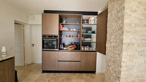 A kitchen with wooden cabinets, a built-in oven, and shelves with various kitchenware and decorative items. - Master villa for 14 people with air conditioning (LES ISSAMBRES)