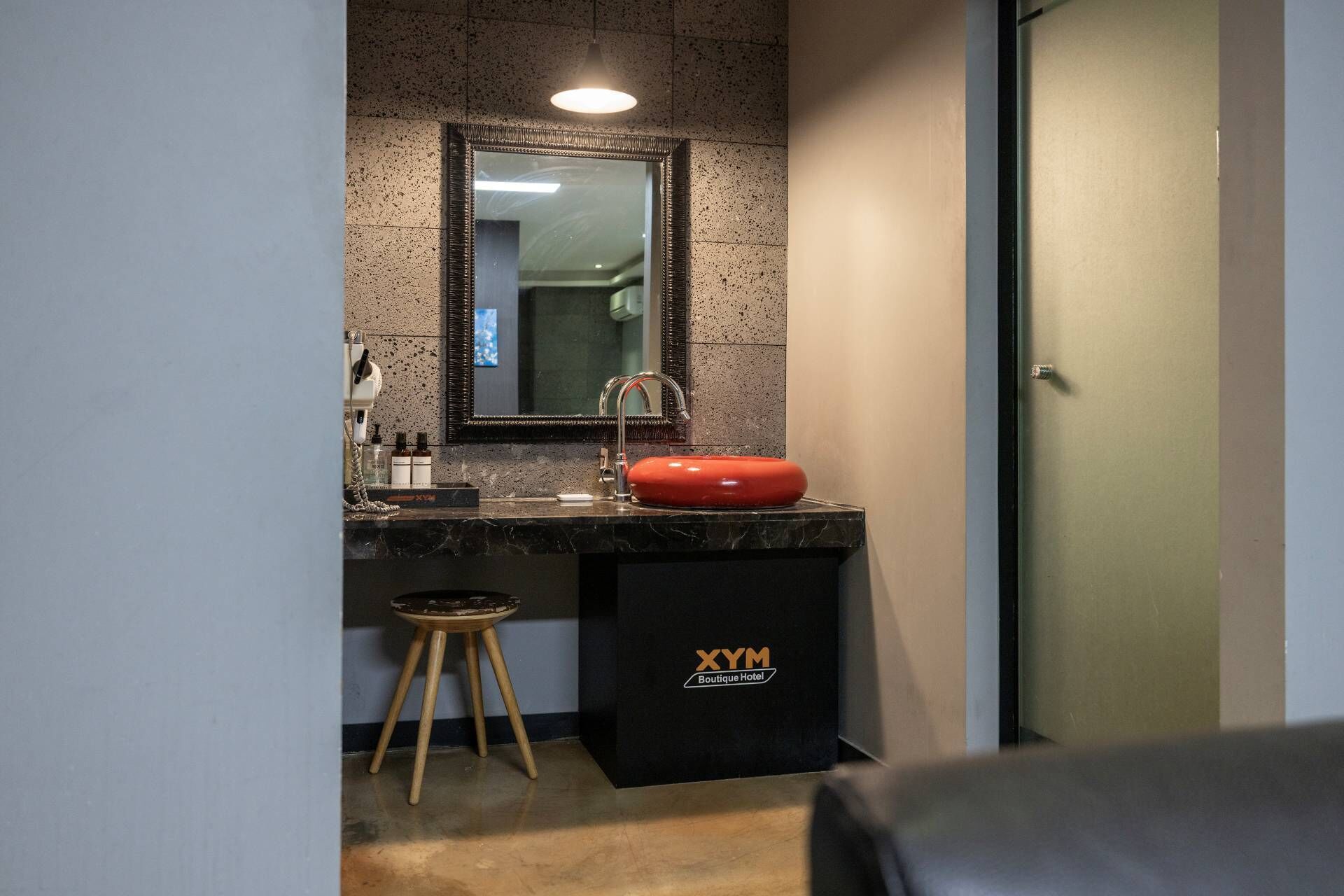 Ein modernes Badezimmer mit einer Granit-Arbeitsplatte, einem roten Waschbecken, einem Spiegel und einem schwarzen Mülleimer mit der Aufschrift 'XYM Boutique Hotel'.