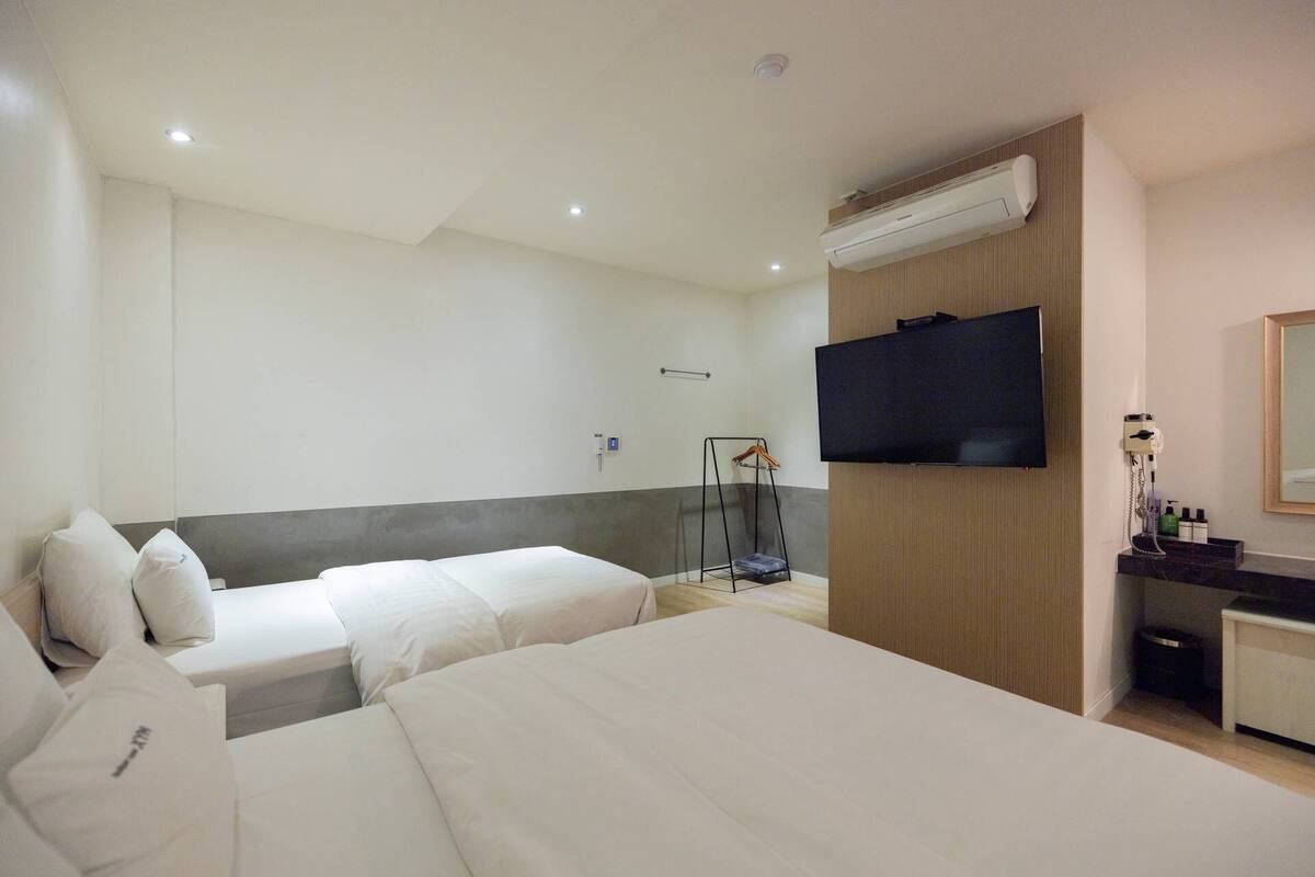 A hotel room with two beds, a TV, a desk with a mirror, and a hanging coat rack.