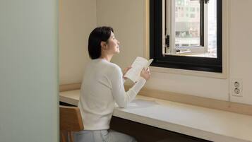 A person sitting on a bench by a window, reading a book.