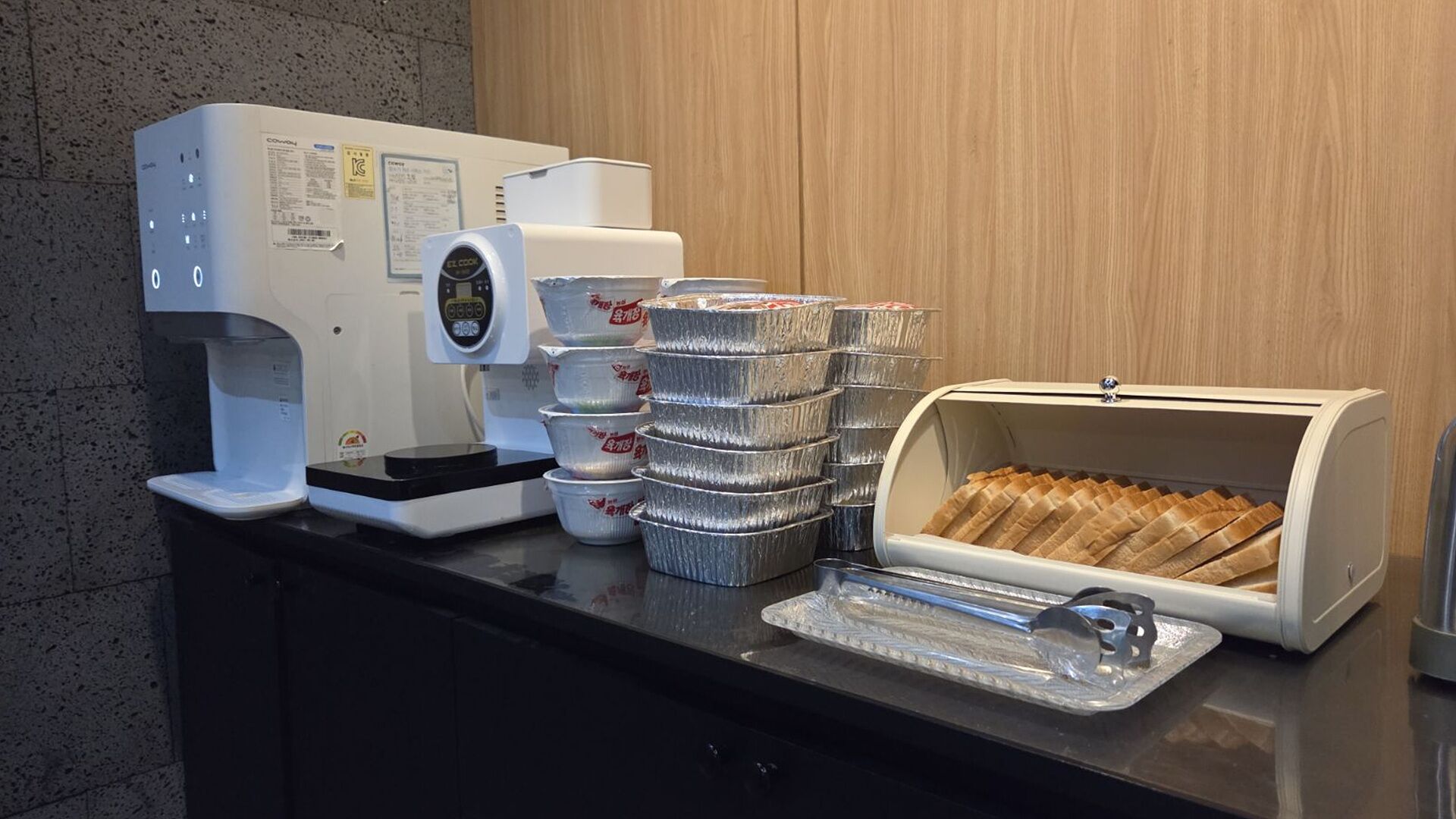 A coffee machine, aluminum foil containers, and a bread box on a counter.