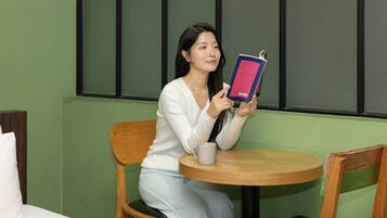 A person seated at a round wooden table with a white mug, holding a book.