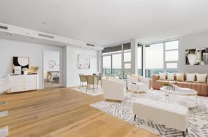 A spacious living room with a large window, a white sofa set, a coffee table, and a wooden floor. - Luxury Living above the Clouds! Best of Vancouver! (Vancouver)