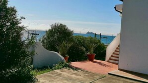 Vista costera con una escalera que conduce a un edificio blanco, rodeado de vegetación y un cielo despejado.