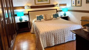 Un dormitorio ordenado con una cama grande, dos mesitas de noche con lámparas, un armario de madera y un techo con una obra de arte enmarcada.