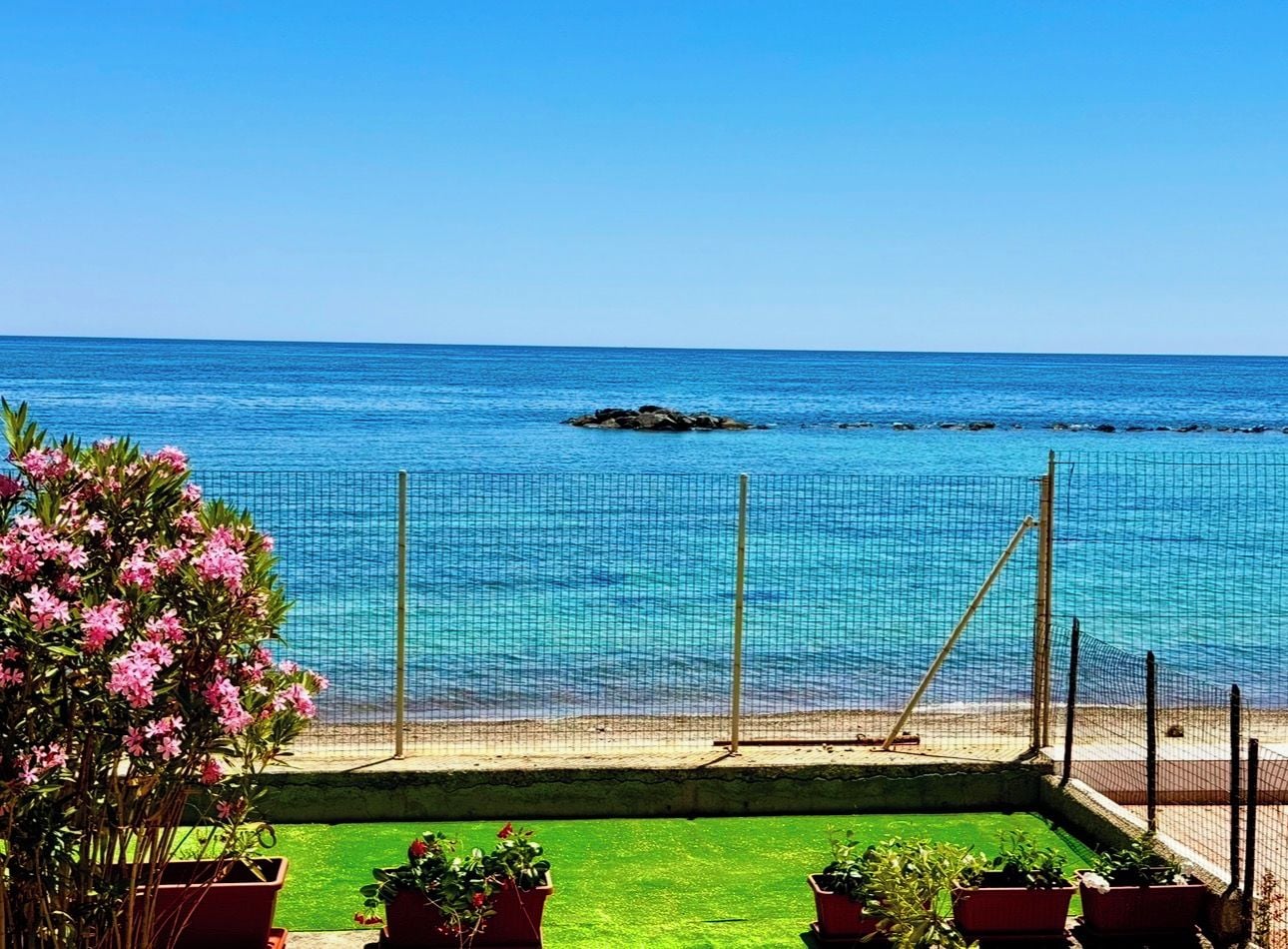 A beach view with a netted area, a grassy foreground, and a clear blue sky.