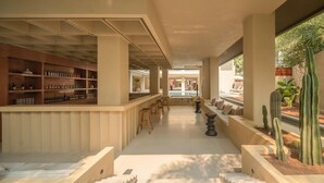 A modern bar area with shelves of bottles, seating, and a view of a pool and garden.