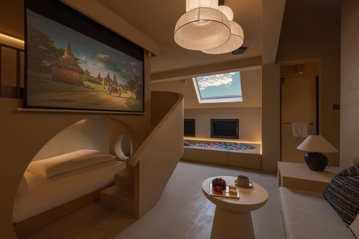 Et moderne hotelværelse med et stort fladskærms-tv, en behagelig sofa, et lille rundt bord med snacks, en trappe og et ovenlys.