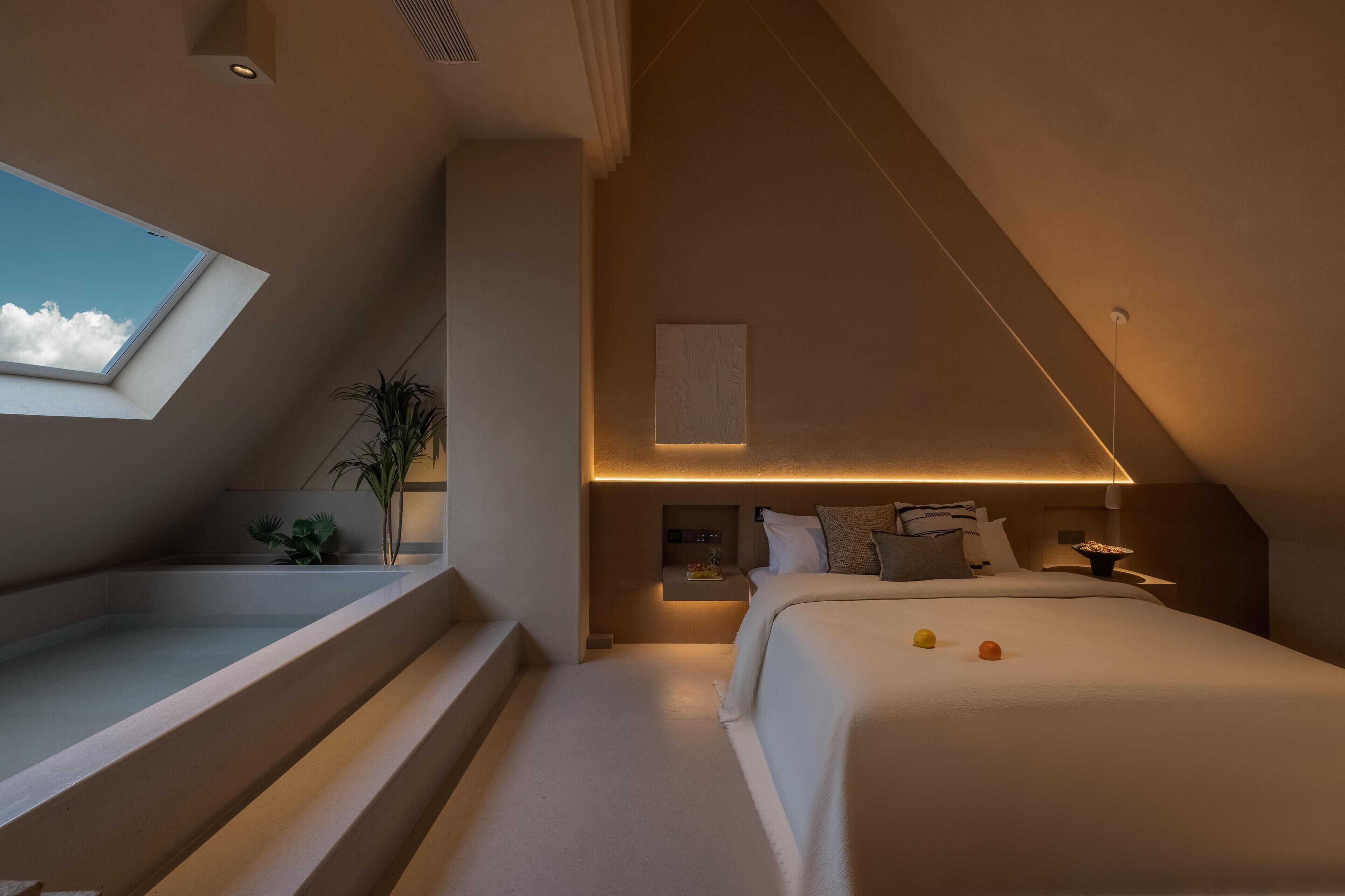 A modern bedroom with a skylight, a built-in bench, and a bedside table with a lamp.