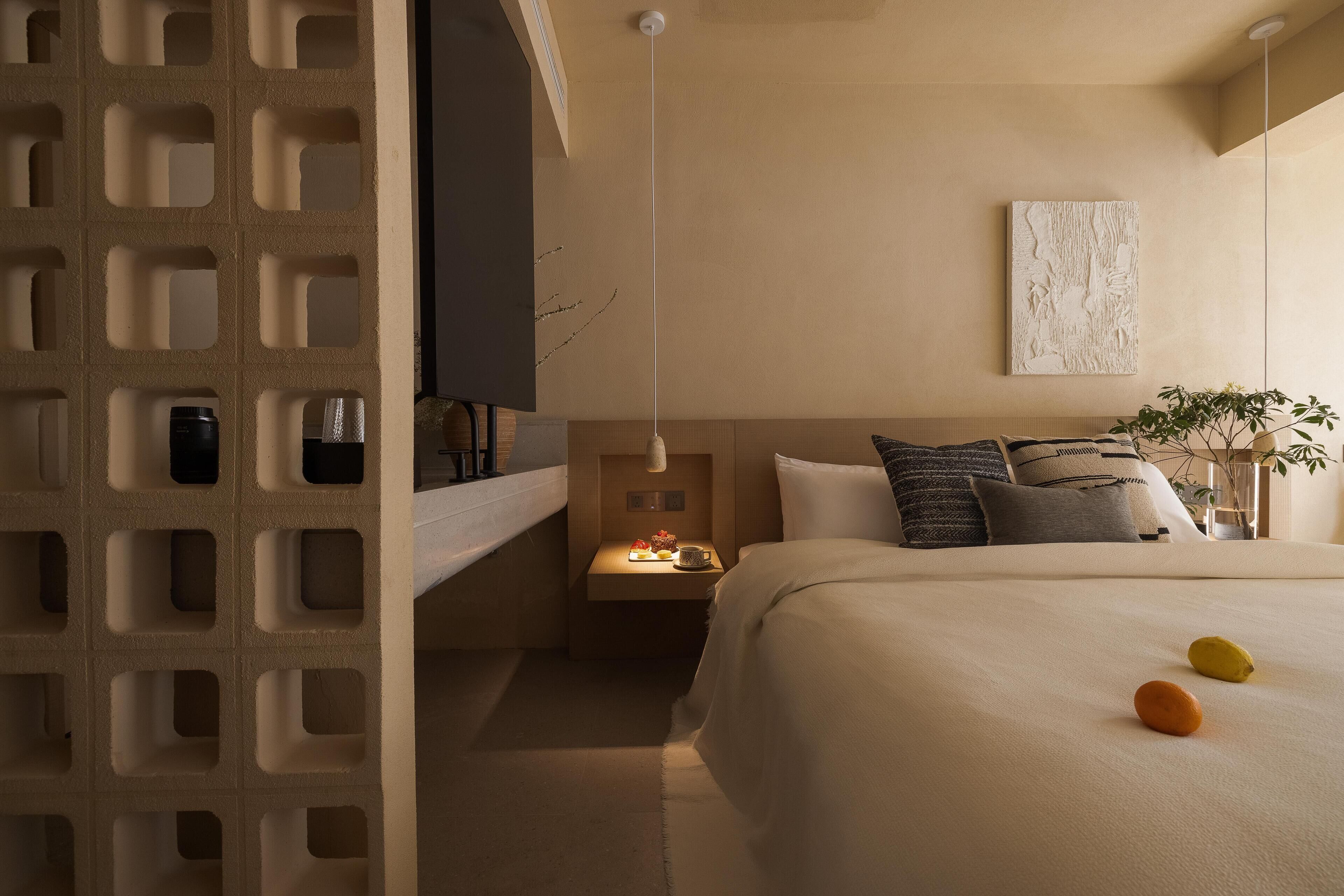 A modern hotel room with a large bed, a small bedside table, a TV, and a wall-mounted artwork.