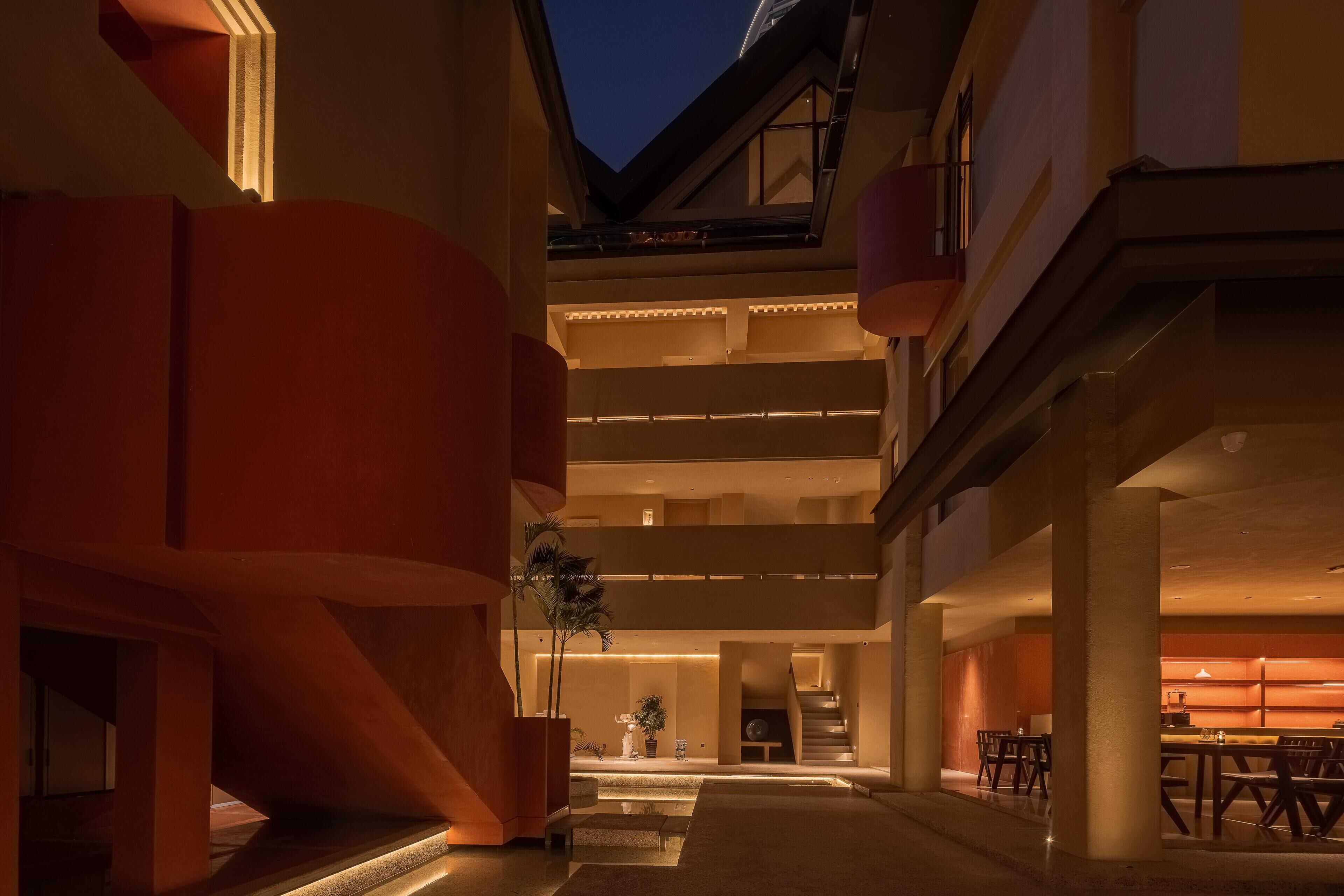 A modern hotel atrium with a central staircase, multiple levels, and a dining area.