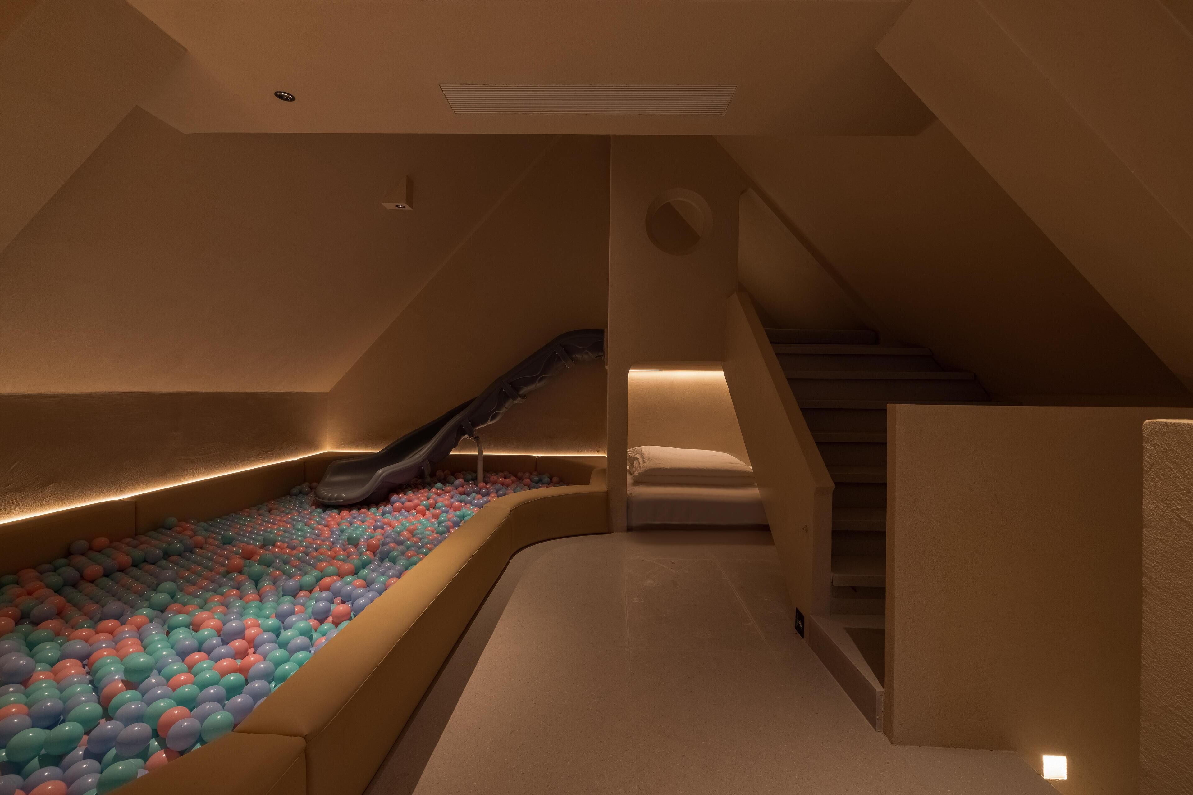 A room with a sloped ceiling, a padded play area with colorful balls, a small slide, and a staircase.