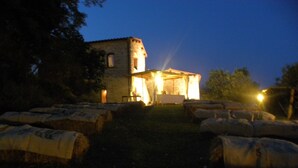 A stone building with a tower, illuminated by warm lights, surrounded by hay bales. - Dream Tuscany (Toscana)