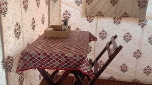 A small room with a table and chairs, a window, and a curtain with a floral pattern. - Chanderi Eco Retreat (Chanderi)
