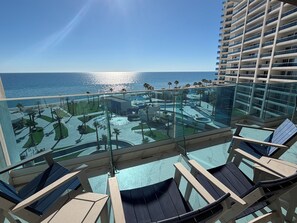 Un balcone con ringhiera in vetro che si affaccia su una piscina e sull'oceano.