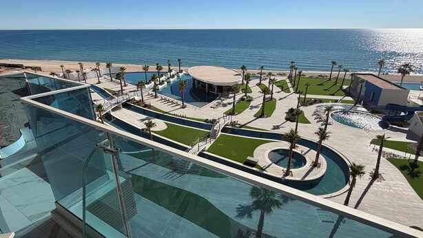 Area piscina resort con diverse piscine, palme e vista sull'oceano.