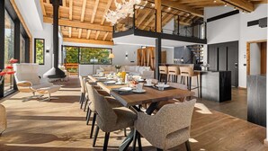 Un vaste espace dédié à la salle à manger, avec une longue table en bois, de nombreuses chaises et un lustre moderne.