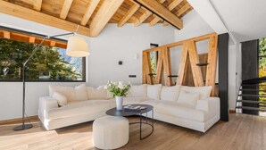 Un salon moderne avec un canapé d’angle blanc, une table basse ronde et une grande fenêtre donnant sur la verdure.