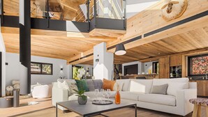 Ein modernes Wohnzimmer mit einem weißen Sofa, einem Couchtisch mit Flasche und Gläsern sowie einer Holzbalkendecke.