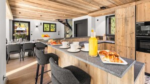 Eine moderne Küche mit Holzboden, einer Bar mit Hockern und einem Essbereich mit Tisch für vier Personen.