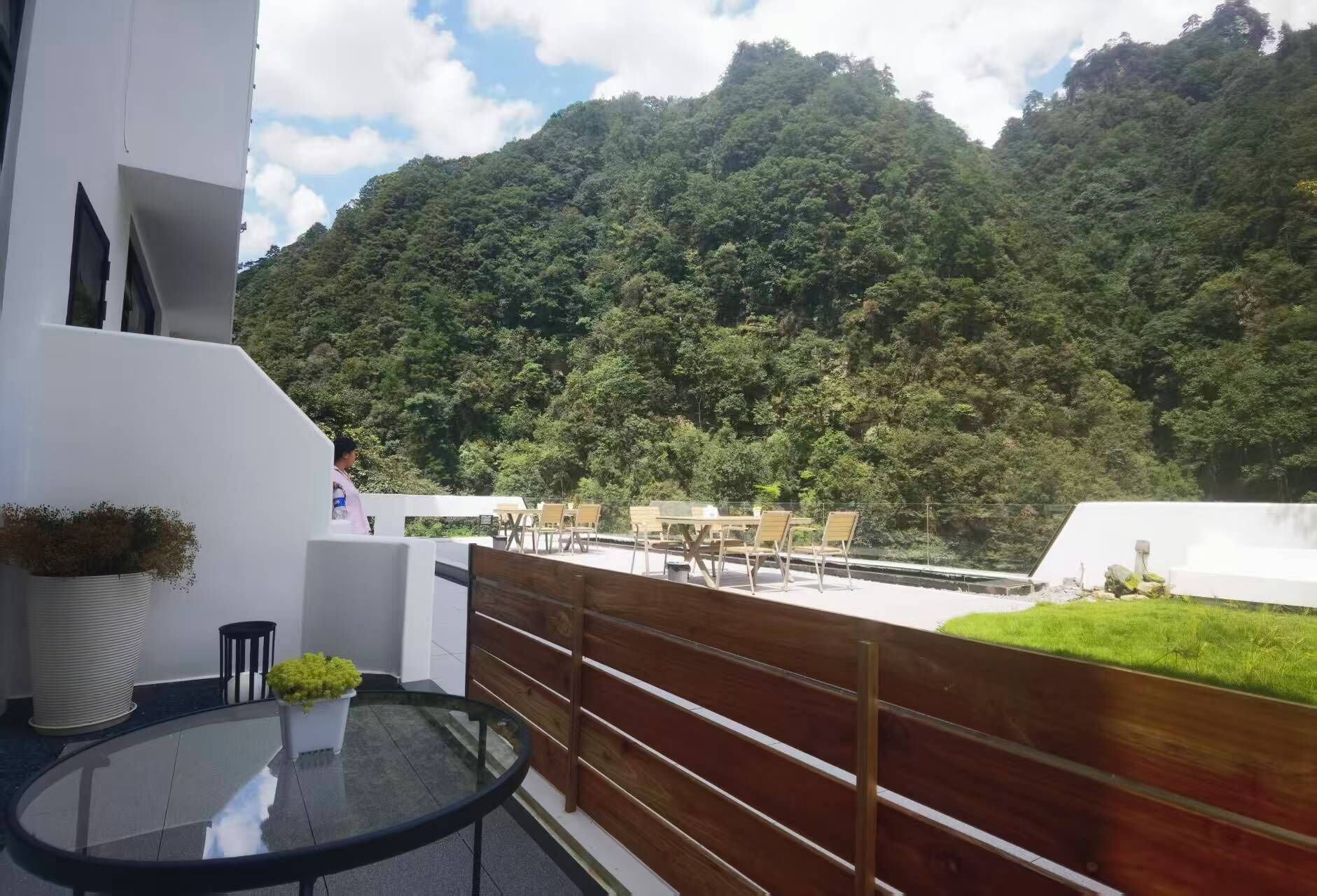 Un balcón con una mesa y sillas de vidrio, con vista a una ladera verde y exuberante.