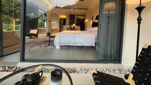Ein modernes Hotelzimmer mit einer großen Glaswand, einem Bett, einem Schreibtisch und einem Sessel.