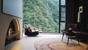 Ein modernes Wohnzimmer mit einem großen Fenster und Blick auf einen bewaldeten Hang.