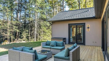 Une terrasse extérieure moderne, avec des meubles en osier, une porte vitrée donnant sur un espace abrité et une plateforme entourée d’arbres.