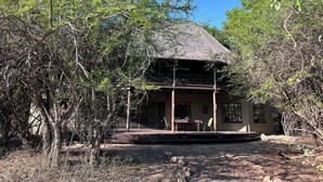 A rustic building with a thatched roof, surrounded by dense foliage. - Reverie Safari Lodge: Exclusive private lodge in Marloth Park (Marloth Park)
