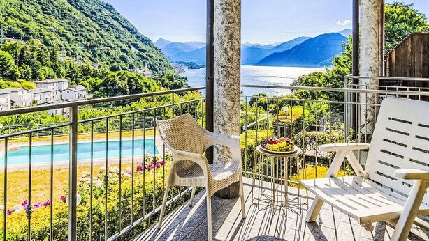 Balcón con vista a un lago y montañas, piscina y mobiliario de exterior.