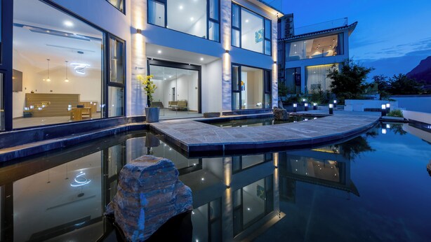 Een modern herenhuis met zwembad, grote ramen en buitenverlichting.