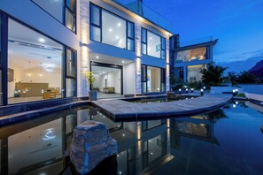 Una casa moderna de dos pisos con piscina, ventanas amplias e iluminación exterior.