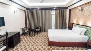 A hotel room with a bed, a desk, two chairs, a TV, and a ceiling fan. - Saltanat Tea Resort Sreemangal (Kamalganj)