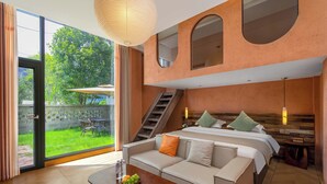 A modern hotel room with a large bed, a sofa, a dining table with fruit, and a view of a garden and staircase. - Riverside Bamboo Frest Hotel (Guilin)