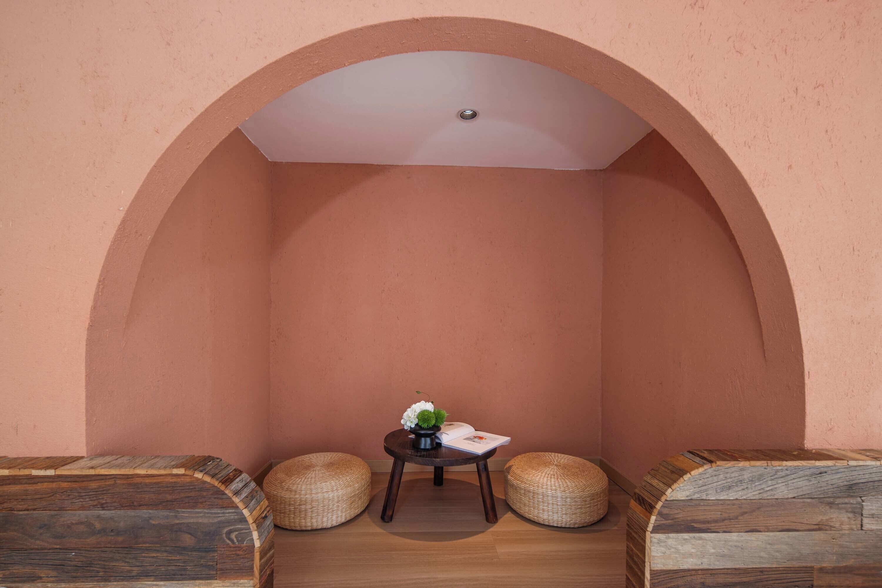 A cozy room with a wooden bench, a small table with a vase and book, and two woven poufs.