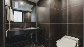 A modern bathroom with a dark tiled wall, a sink with a mirror above it, and a toilet.