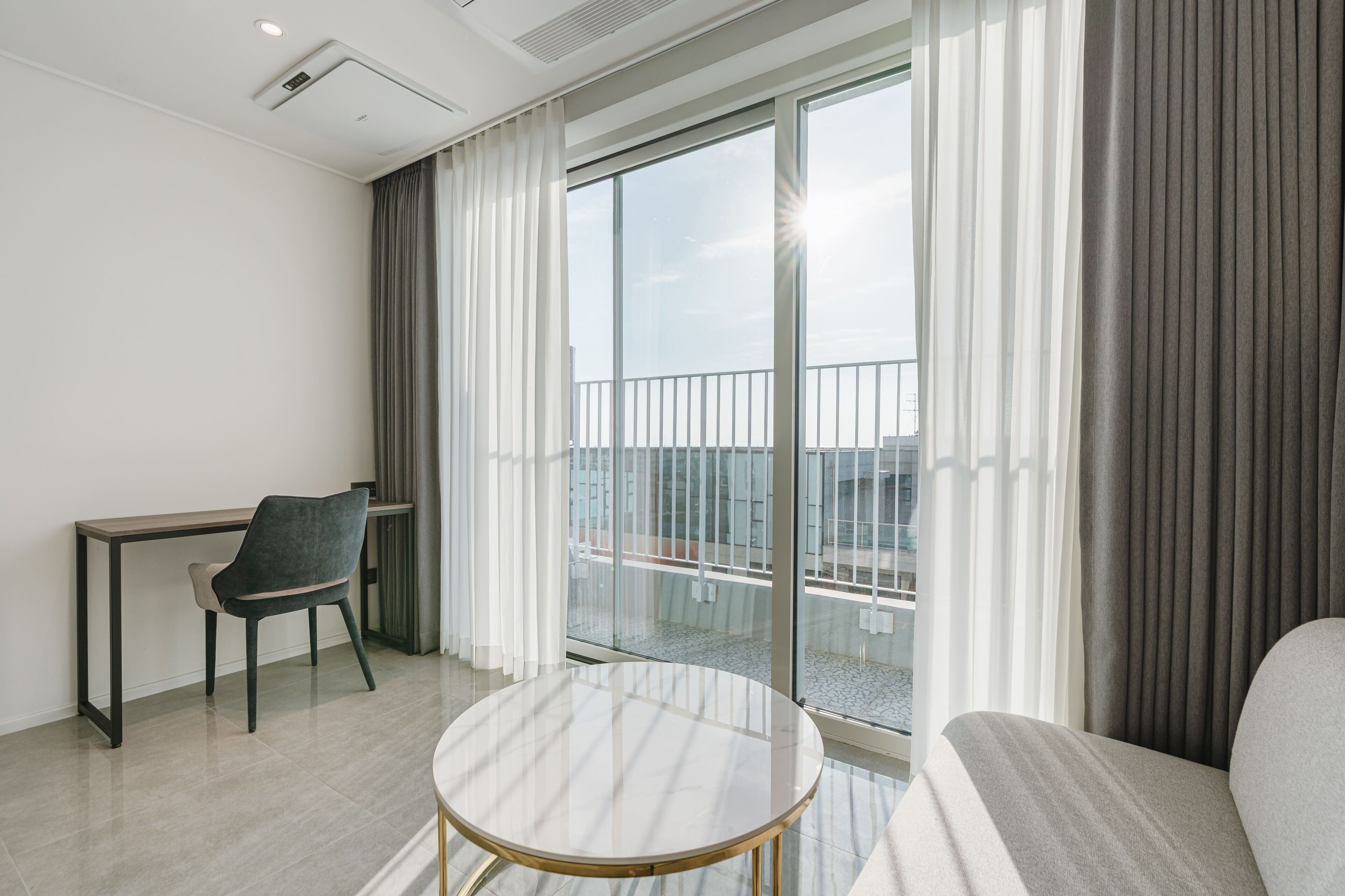 Una habitación de hotel moderna con balcón, una mesa redonda, una silla y un sofá.