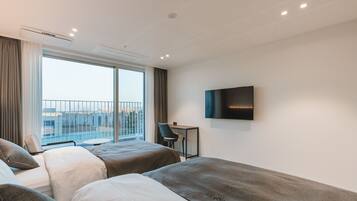 Ein Hotelzimmer mit zwei Betten, einem Schreibtisch, einem Stuhl, einem Fernseher und einem Balkon mit Aussicht.