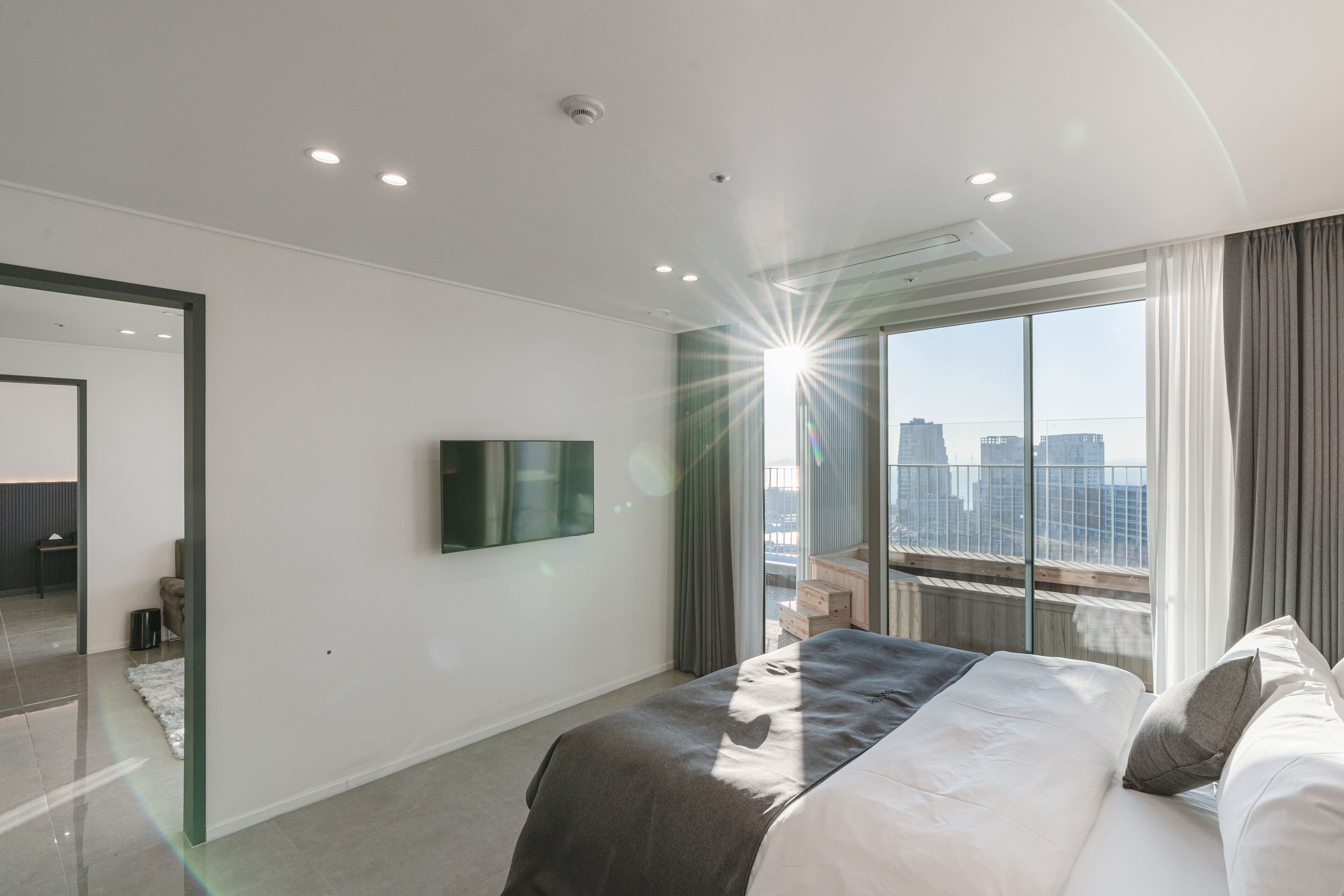 Una habitación de hotel moderna con una cama grande, un televisor de pantalla plana montado en la pared y vistas a la ciudad a través de amplios ventanales.