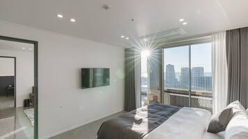 Una habitación de hotel moderna con una cama grande, un televisor de pantalla plana montado en la pared y vistas a la ciudad a través de amplios ventanales.