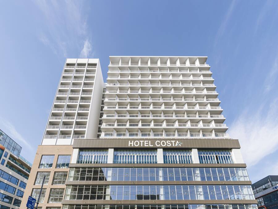 A modern hotel building with multiple floors, large windows, and a prominent sign reading "HOTEL COSTA".