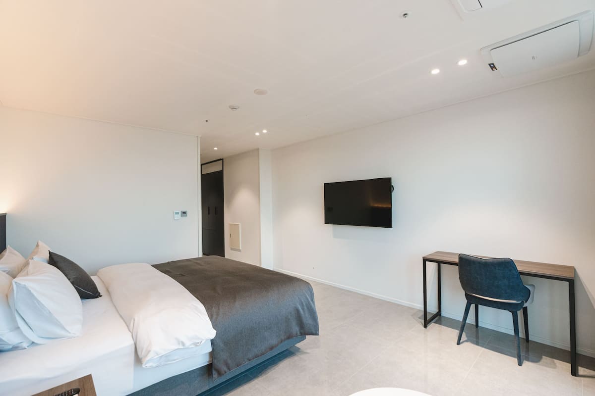 Ein modernes Hotelzimmer mit Bett, Schreibtisch, Stuhl und einem an der Wand befestigten Flachbildfernseher.