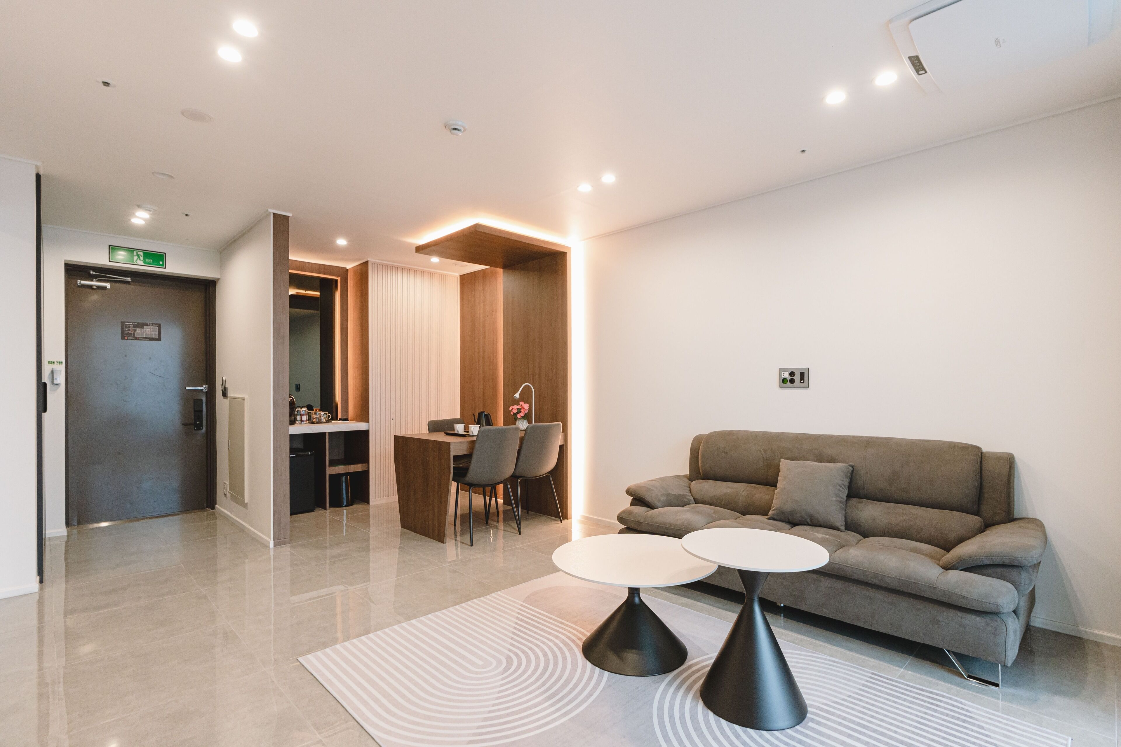 A modern hotel lobby with a sofa, two round tables, a dining area, and a reception desk.
