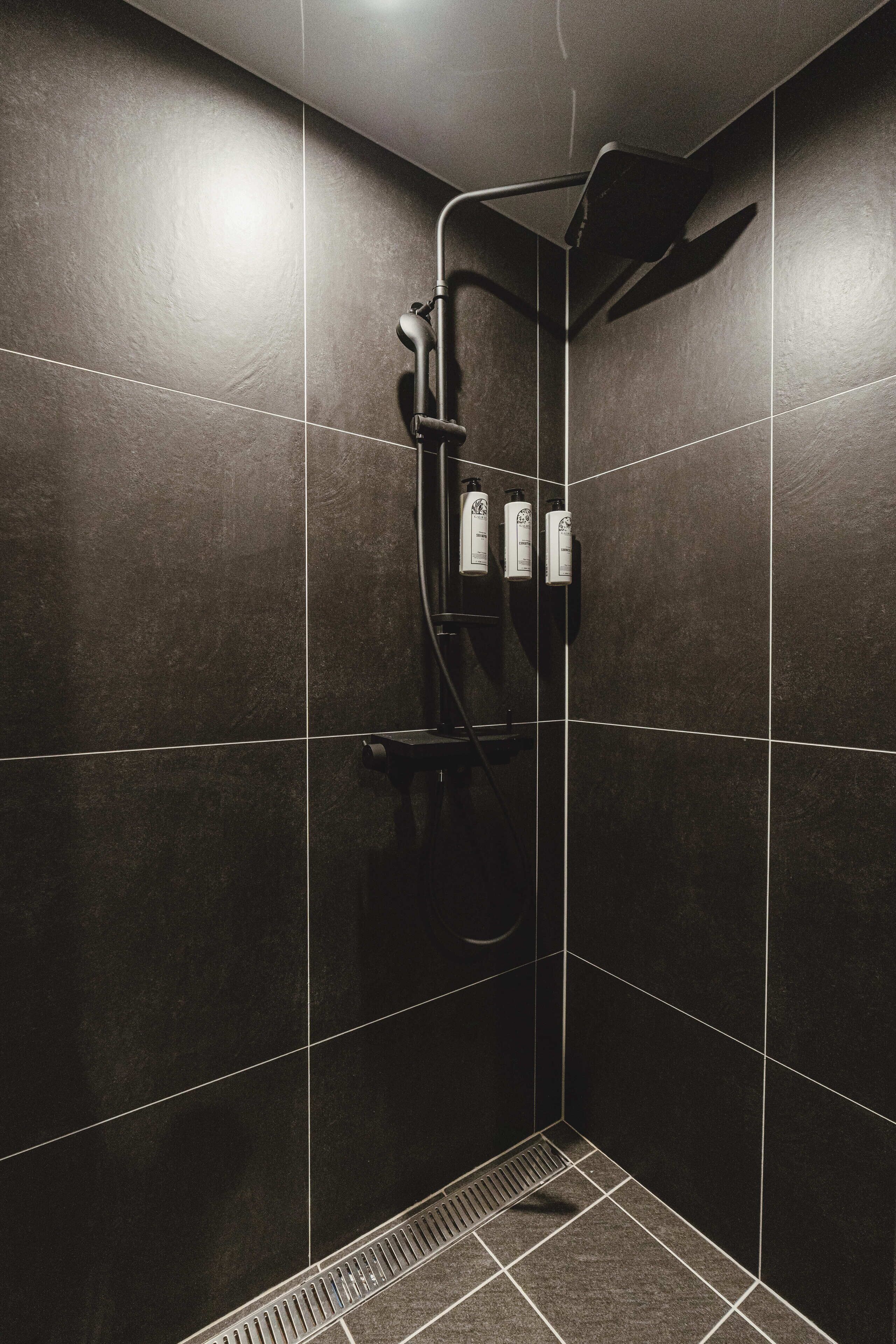 A modern shower area with dark tiles and a handheld showerhead.