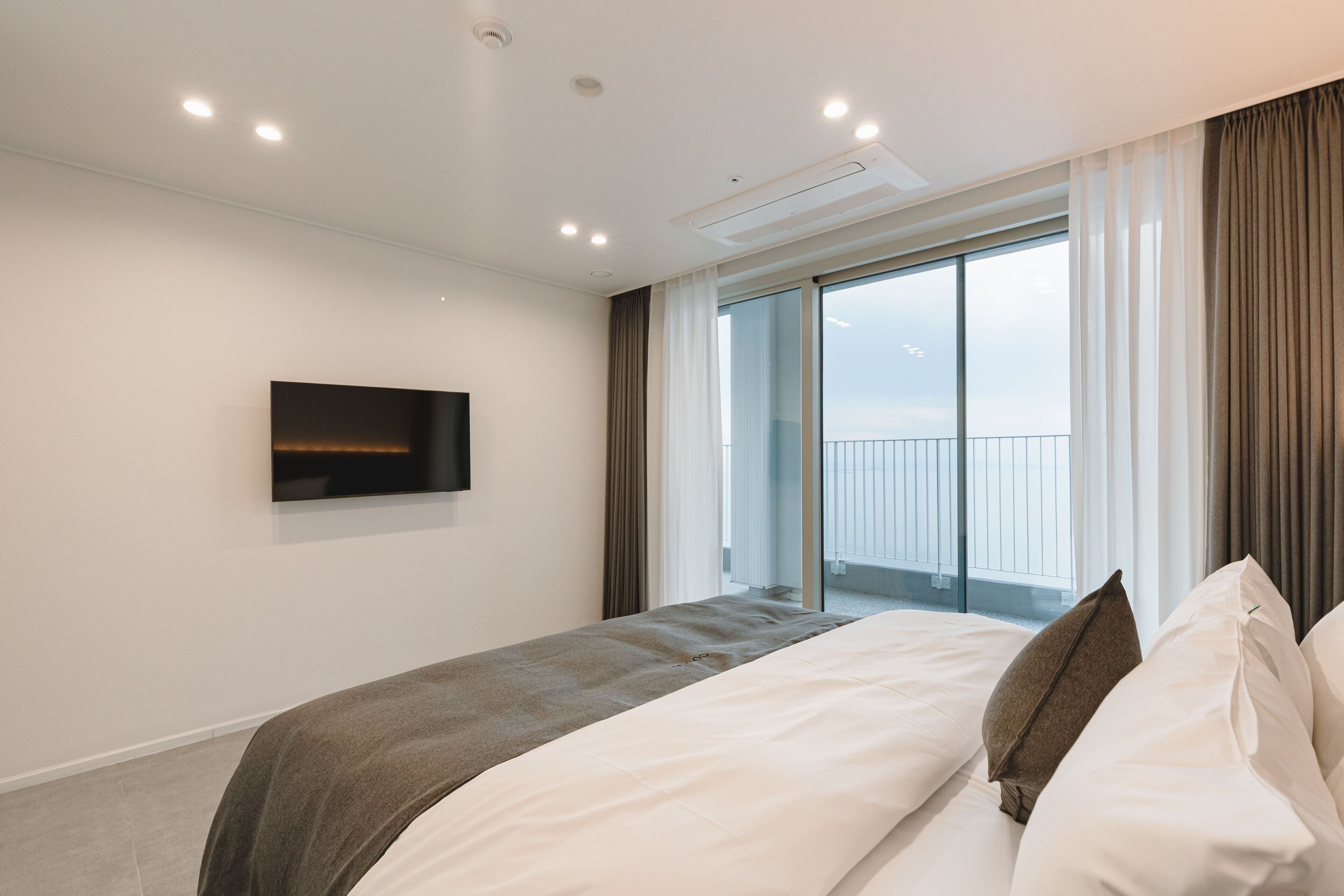 Ett modernt hotellrum med en stor säng, en platt-TV som är monterad på väggen och en balkong med utsikt över staden.