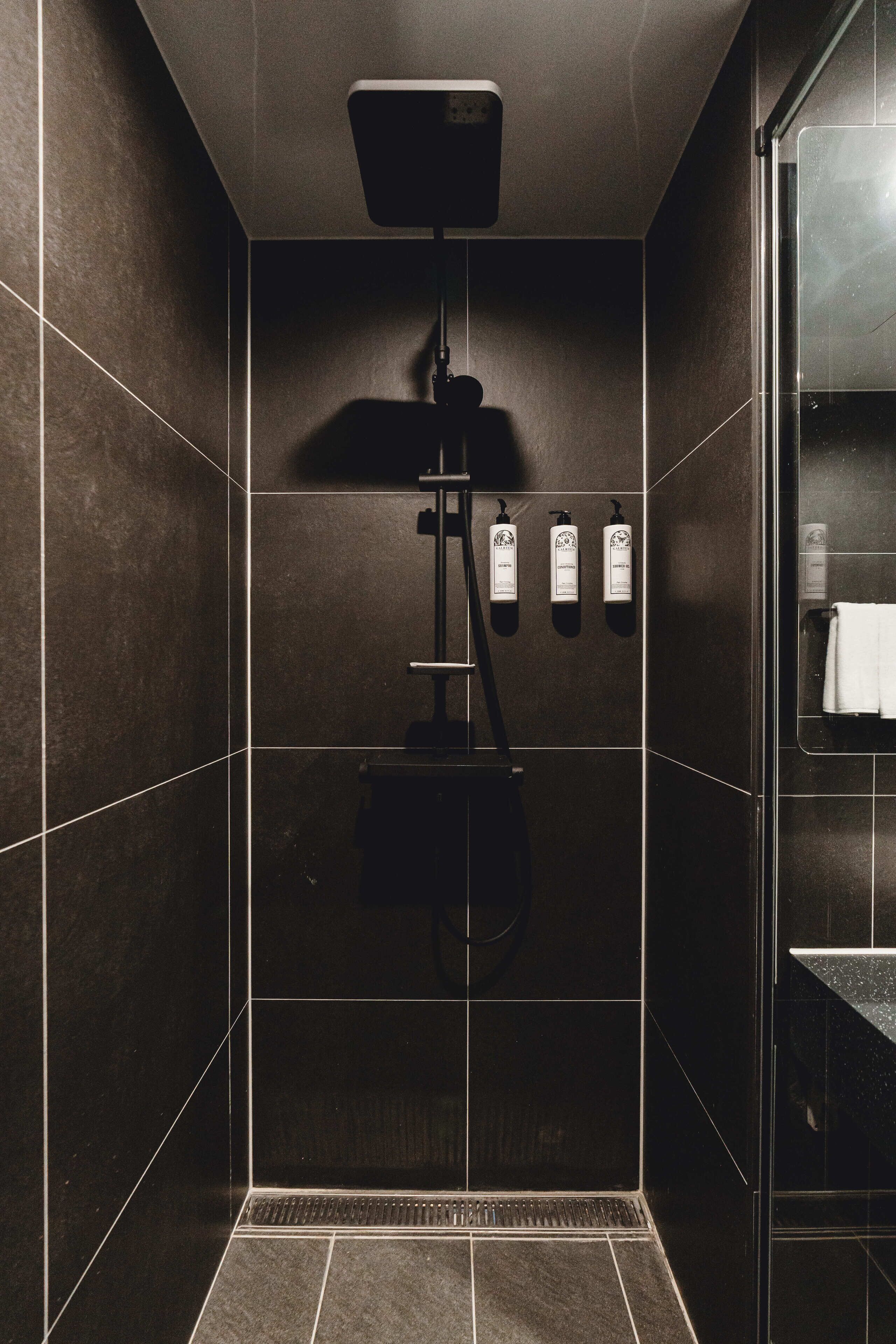 A modern shower area with a control panel, a towel rack, and toiletries.