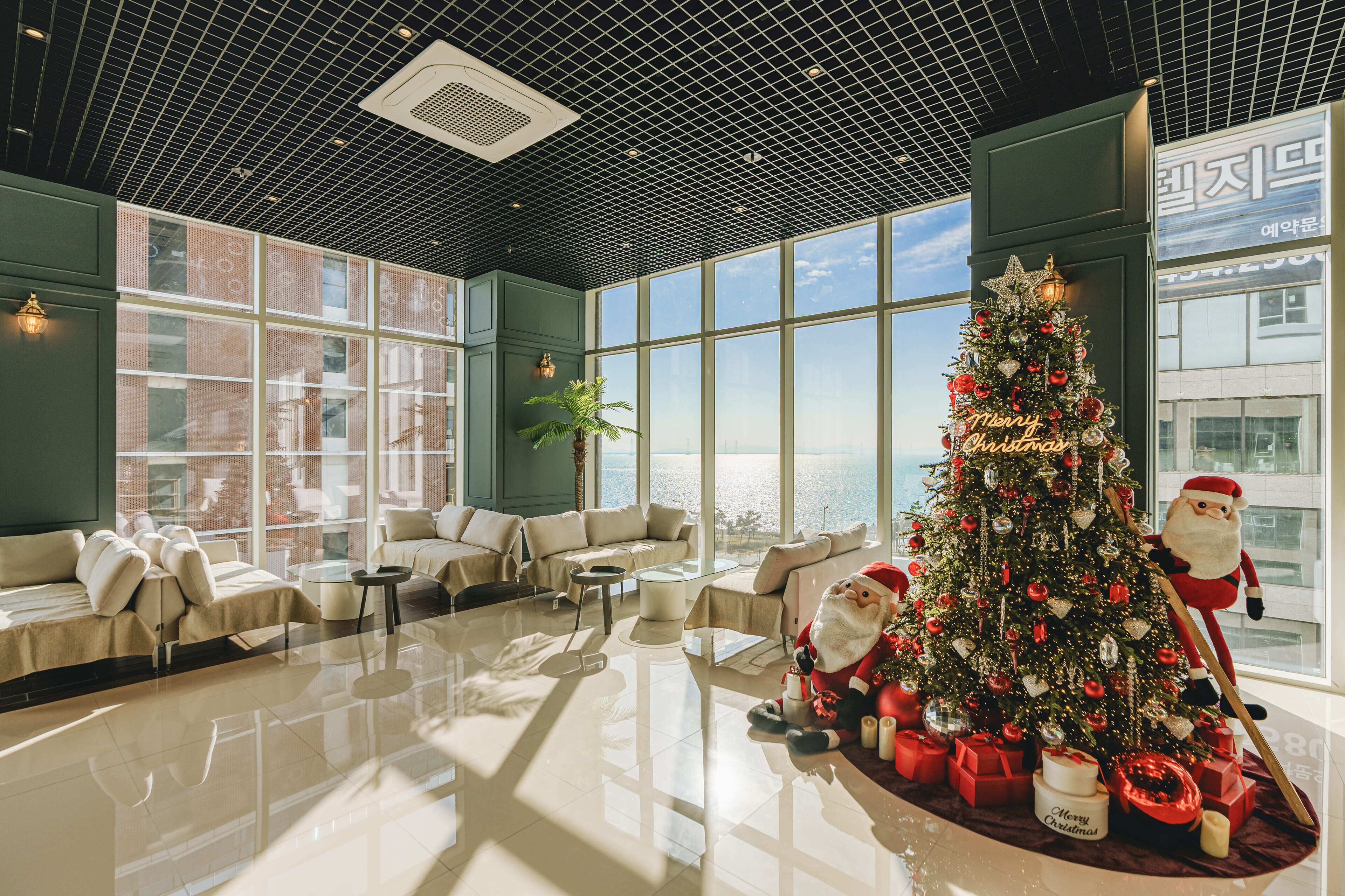 A modern hotel lobby with a large Christmas tree, plush seating, and a view of the city.