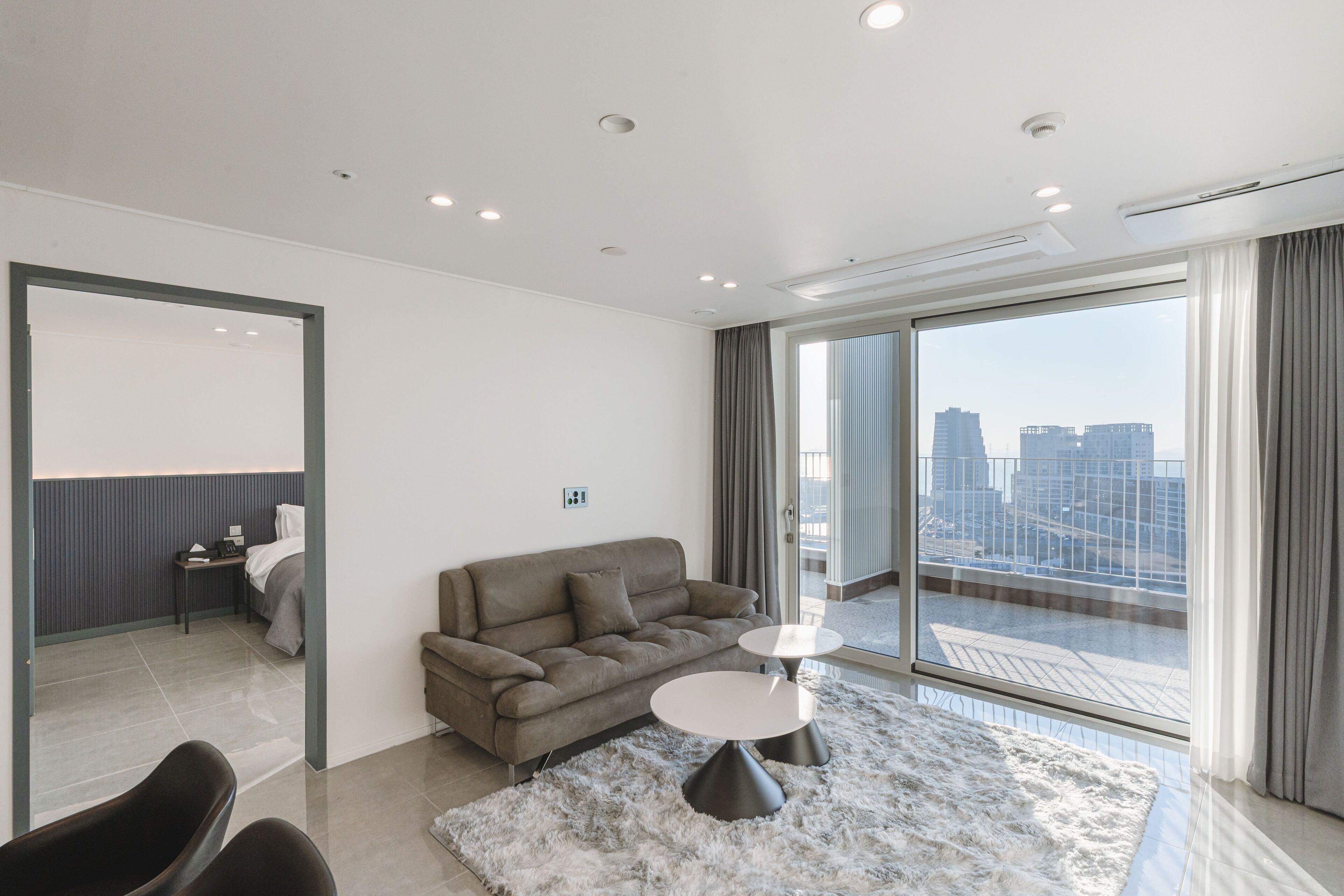 A modern living room with a sofa, two side tables, and a large window with a city view.