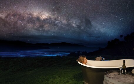 A person relaxing in a bathtub under a starry night sky with a view of the Milky Way.
