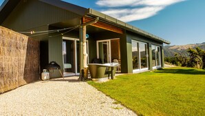 Et moderne hus med stor terrasse, grill og udsigt til bakker.